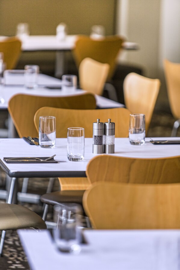 Un restaurante con mesas dispuestas para comer, incluyendo vasos, cubiertos y condimentos.