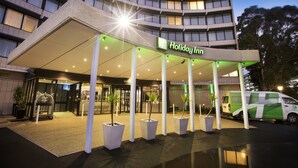 A Holiday Inn hotel entrance with a covered walkway, potted plants, and a van parked outside.