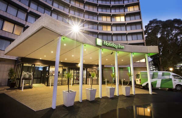 A Holiday Inn hotel entrance with a covered walkway, potted plants, and a van parked outside.