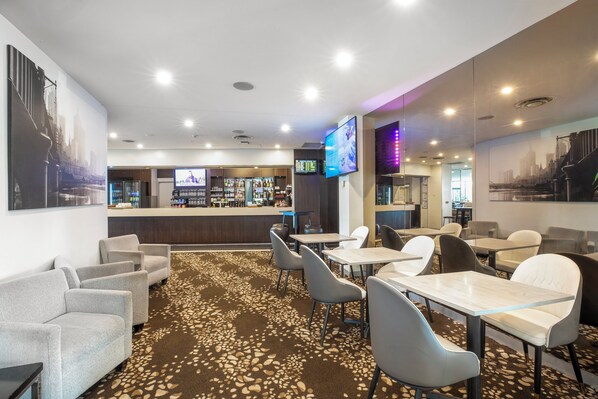 Un vestíbulo de hotel con una zona de bar, disposición de asientos y alfombra estampada.
