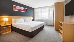 A modern hotel room with a large bed, bedside tables, a flat-screen TV, and a large window with curtains.