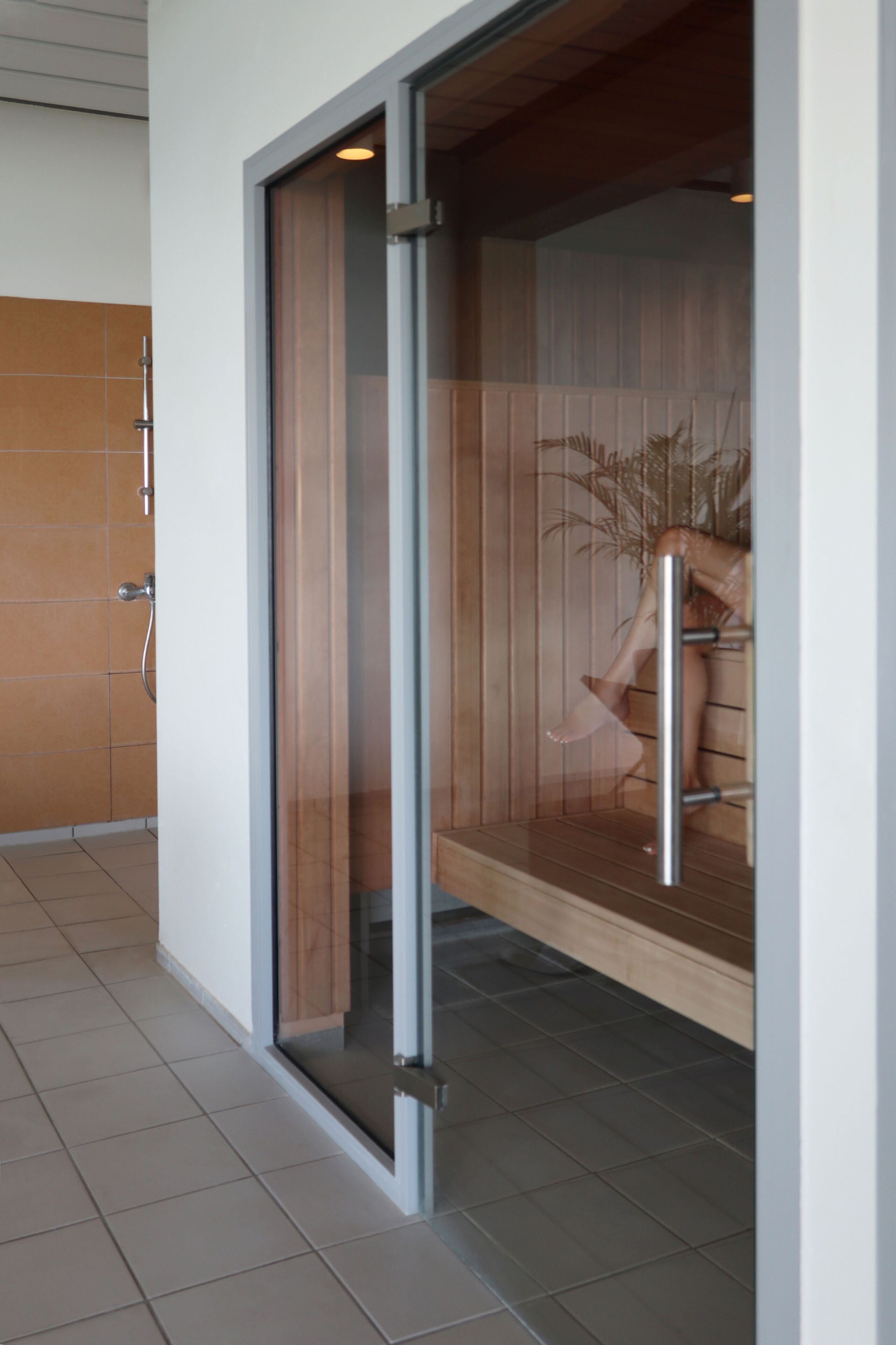 Une salle de bain moderne dotée d’une porte en verre, de lambris en bois et d’un porte-serviettes apparent.