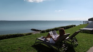 Una mujer leyendo un libro en una silla de descanso junto al mar.