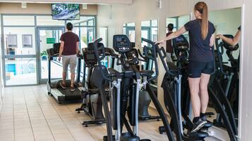 Une salle de sport équipée de plusieurs tapis de course et d’un écran de télévision diffusant les actualités.
