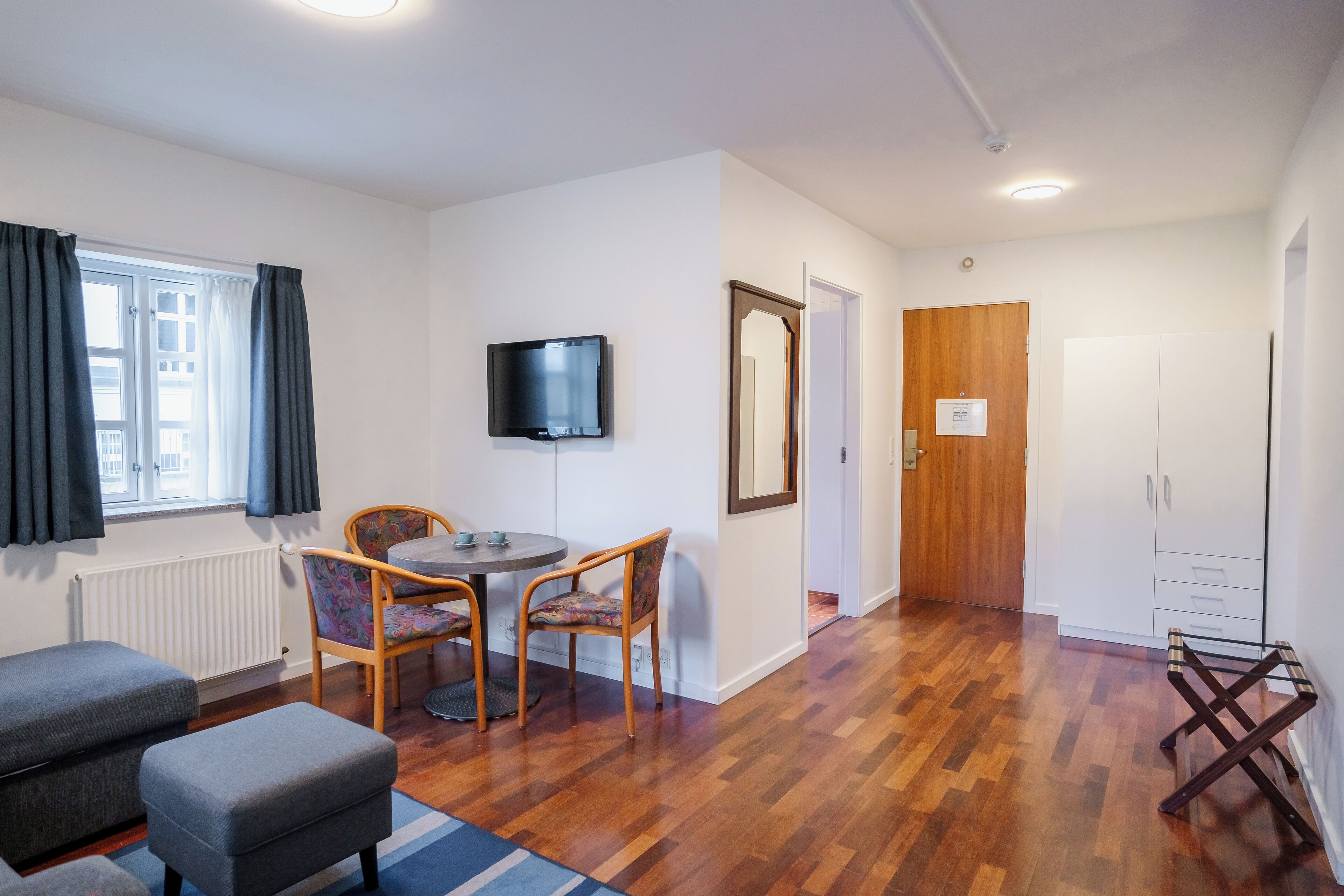 Une chambre moderne avec un plancher en bois, une table à manger avec des chaises, un téléviseur et une armoire.