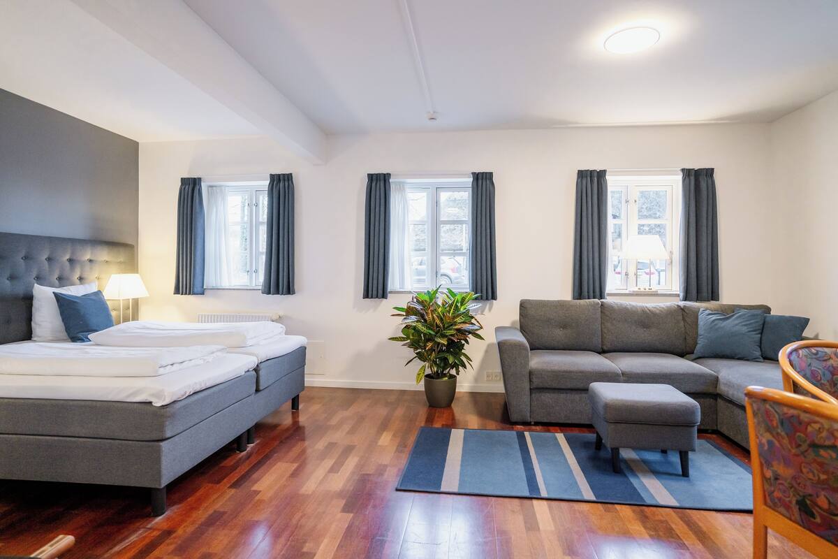 A modern hotel room with a bed, sofa, and a potted plant.