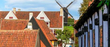 Un village européen traditionnel avec des maisons à colombages, un moulin à vent, des rues pavées et une enseigne indiquant « S.A. Bang ».