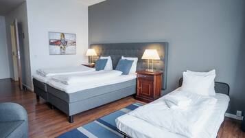 Une chambre d’hôtel avec deux lits, un plancher en bois, un tapis à rayures bleues et un tableau au mur.