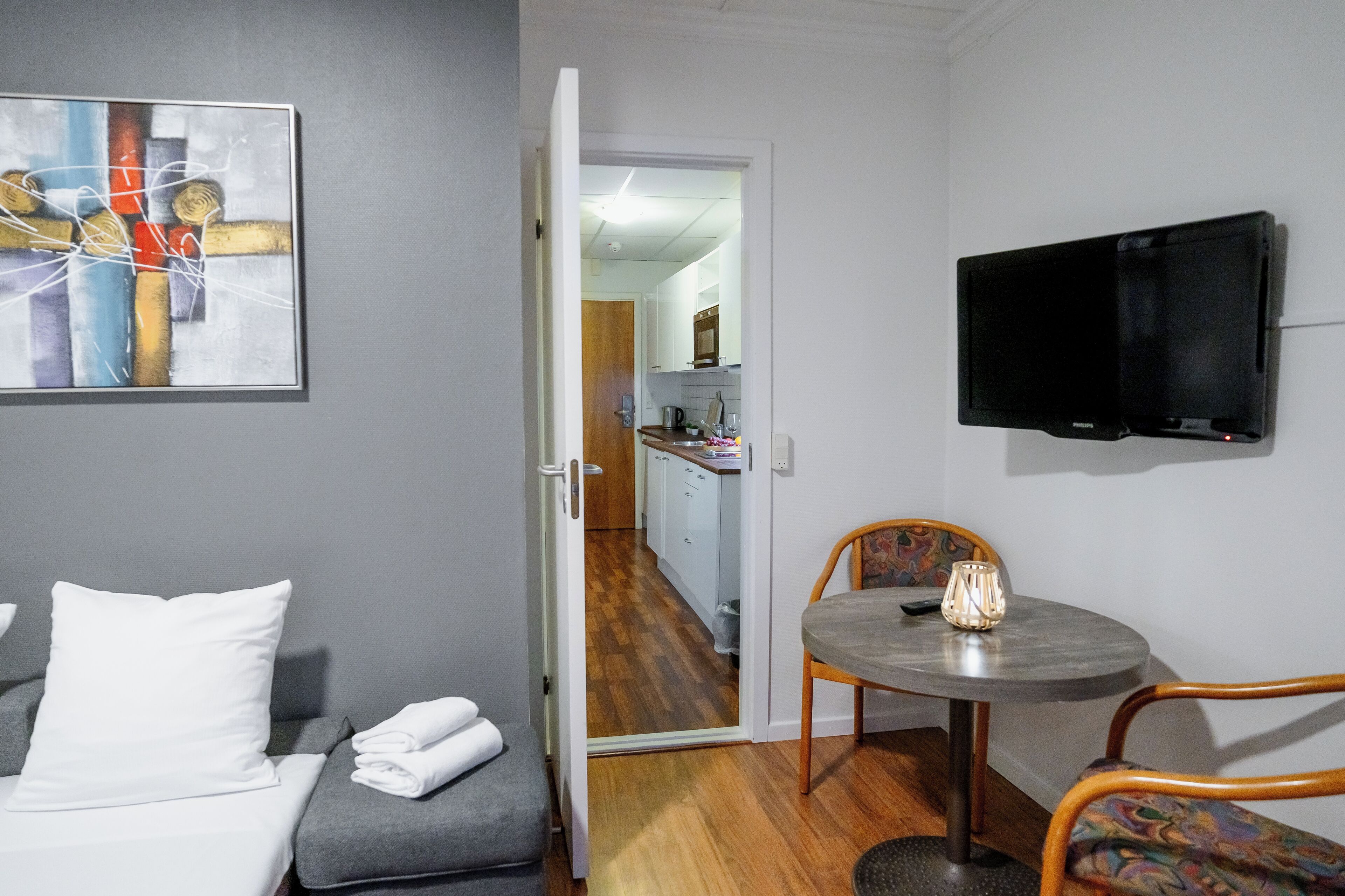 Habitación de hotel con cama, una mesa de comedor con una silla, un televisor montado en la pared y un cuadro colgado.