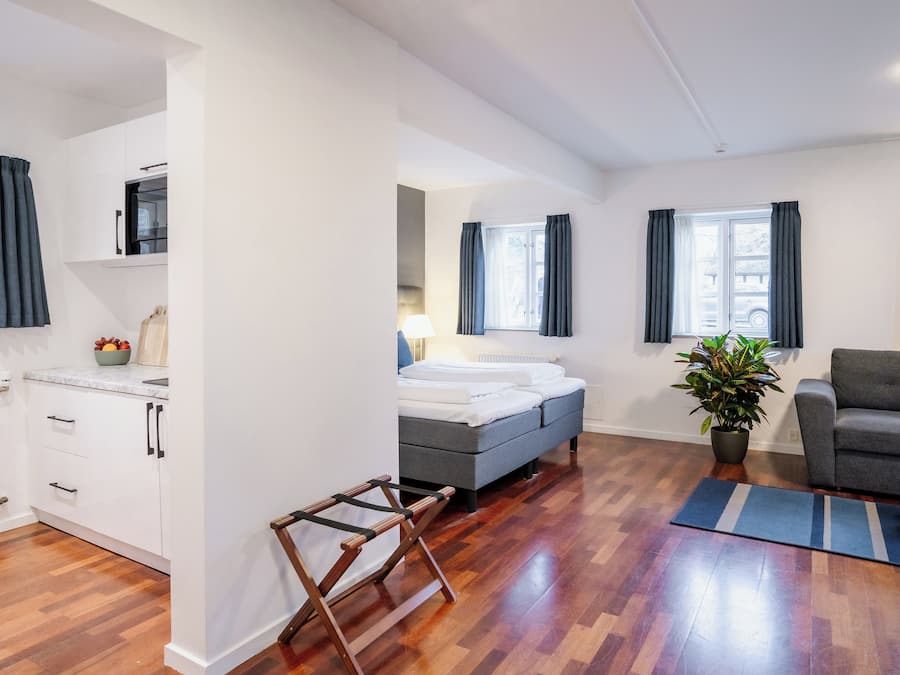 A modern apartment with a bed, grey sofa, wooden flooring, white walls, and a potted plant.