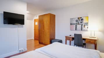 Habitación de hotel con cama, escritorio, silla, televisor, armario y una obra de arte en la pared.