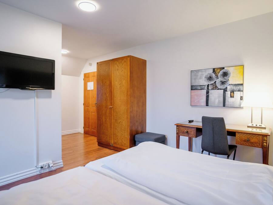 Habitación de hotel con cama, escritorio, silla, televisor, armario y una obra de arte en la pared.