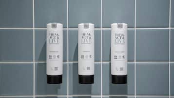 Three bottles of THINK ACT & LIVE products: SHOWER GEL, SHAMPOO, and CONDITIONER, arranged on a tiled wall.