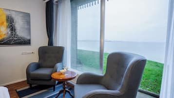 Una habitación con dos sillones grises, una mesita redonda con un bol y un vaso, y un cuadro en la pared.