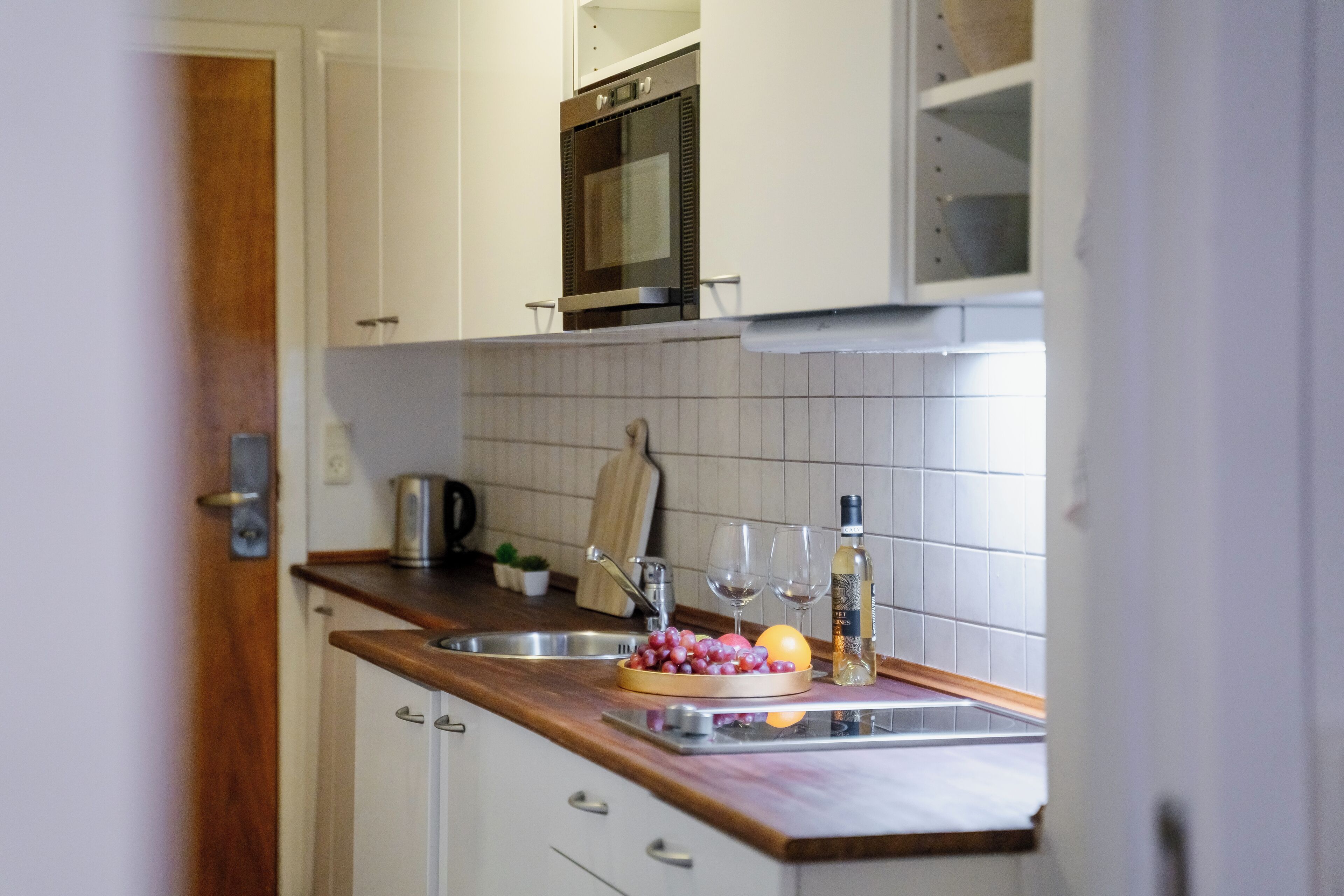 A kitchen with white cabinets, a wooden countertop, a stainless steel sink, and a built-in oven.