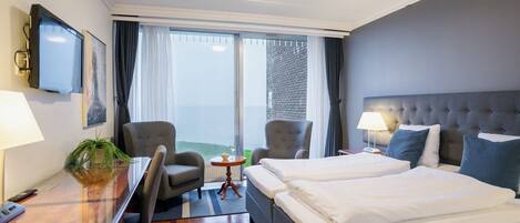 Habitación de hotel con una cama grande, dos sillones, un escritorio con lámpara, televisor y vistas al exterior.