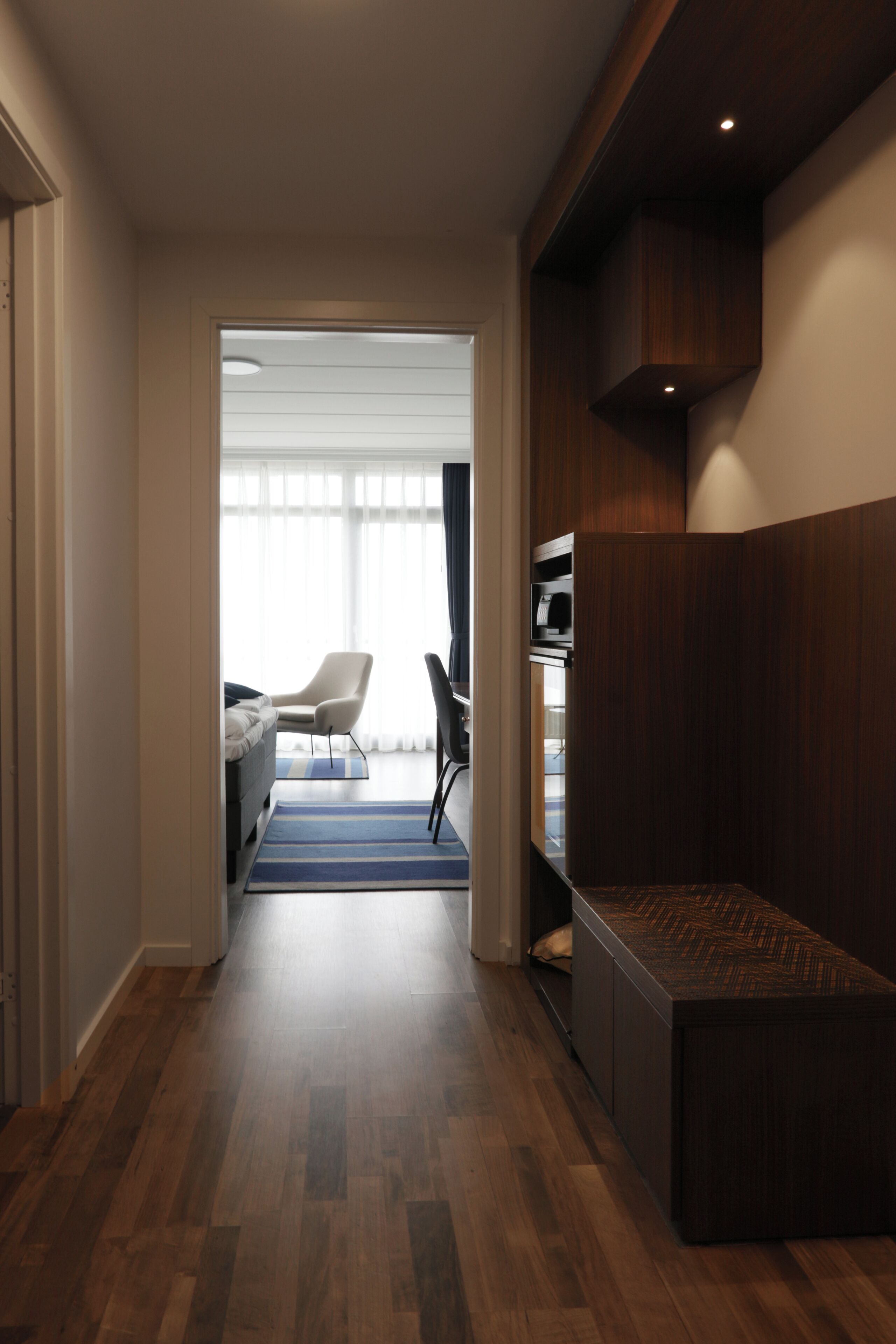 Un pasillo de hotel con suelo de madera, un área de descanso y vistas a una habitación con una cama y una silla.