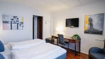 Habitación de hotel con dos camas, un escritorio, una silla, un televisor y obras de arte en las paredes.