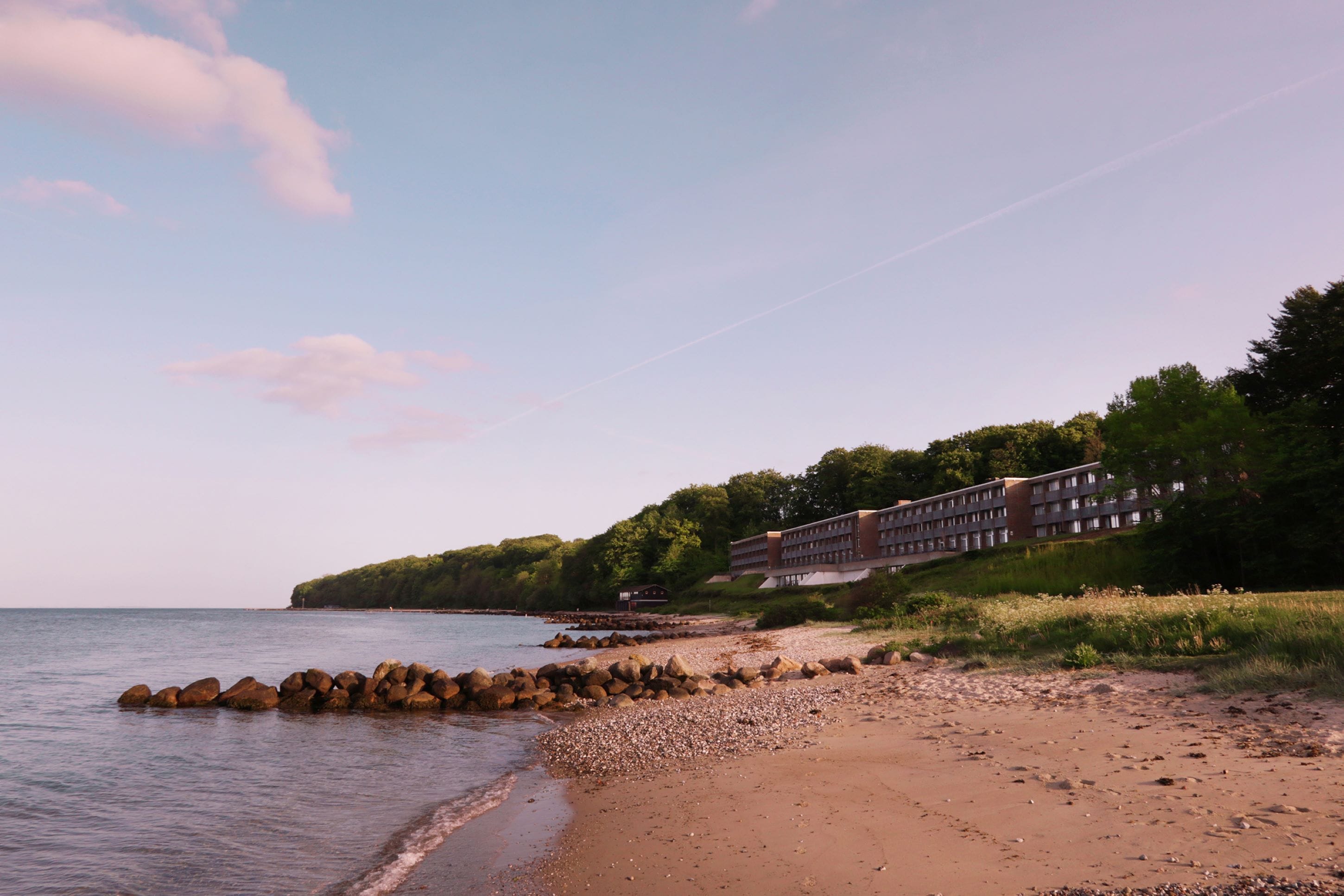 A coastal hotel with a rocky shoreline, a building with multiple floors, and a view of the sea.