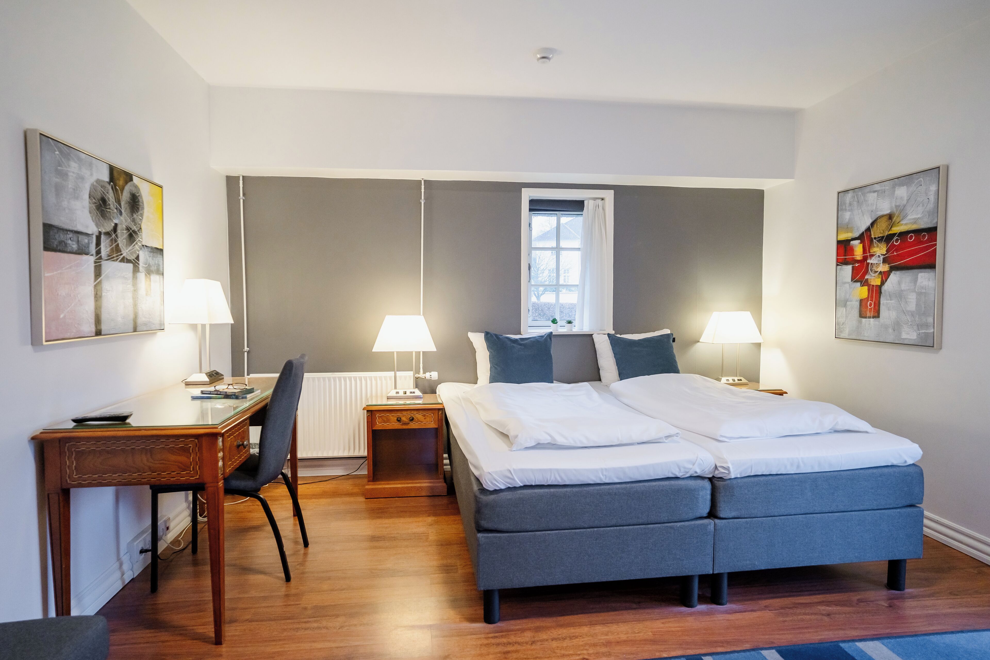 A modern bedroom with a large bed, two bedside tables with lamps, a desk, and chairs.