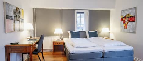 Un dormitorio moderno con una cama grande, dos mesitas de noche con lámparas, un escritorio y sillas.