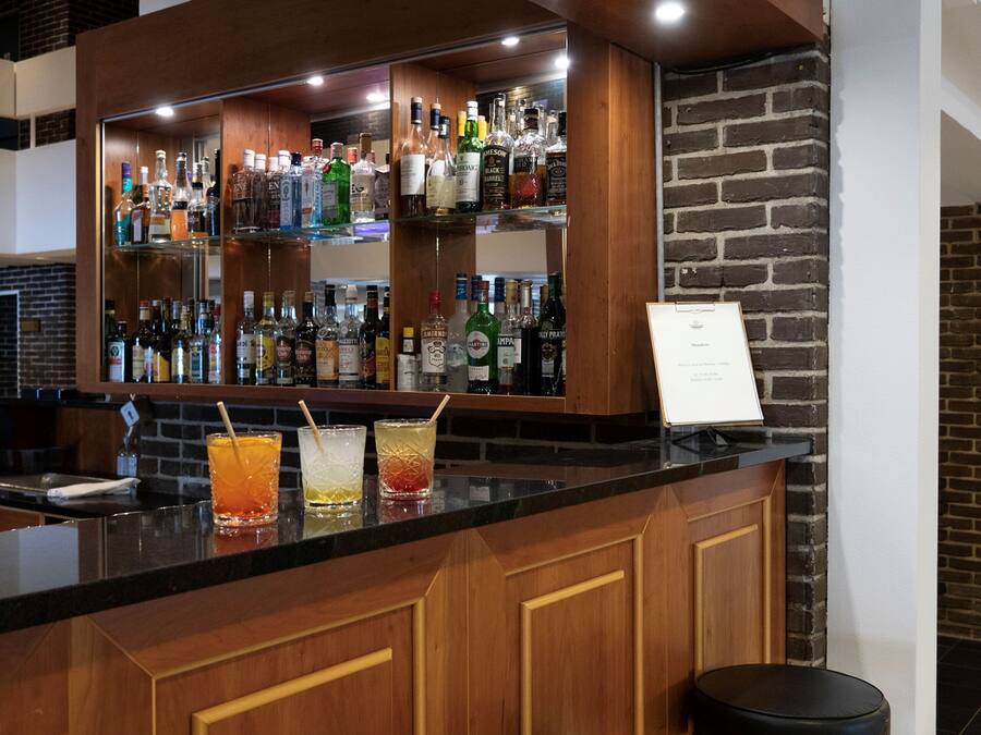 A bar area with a wooden counter, multiple liquor bottles, and three stools.