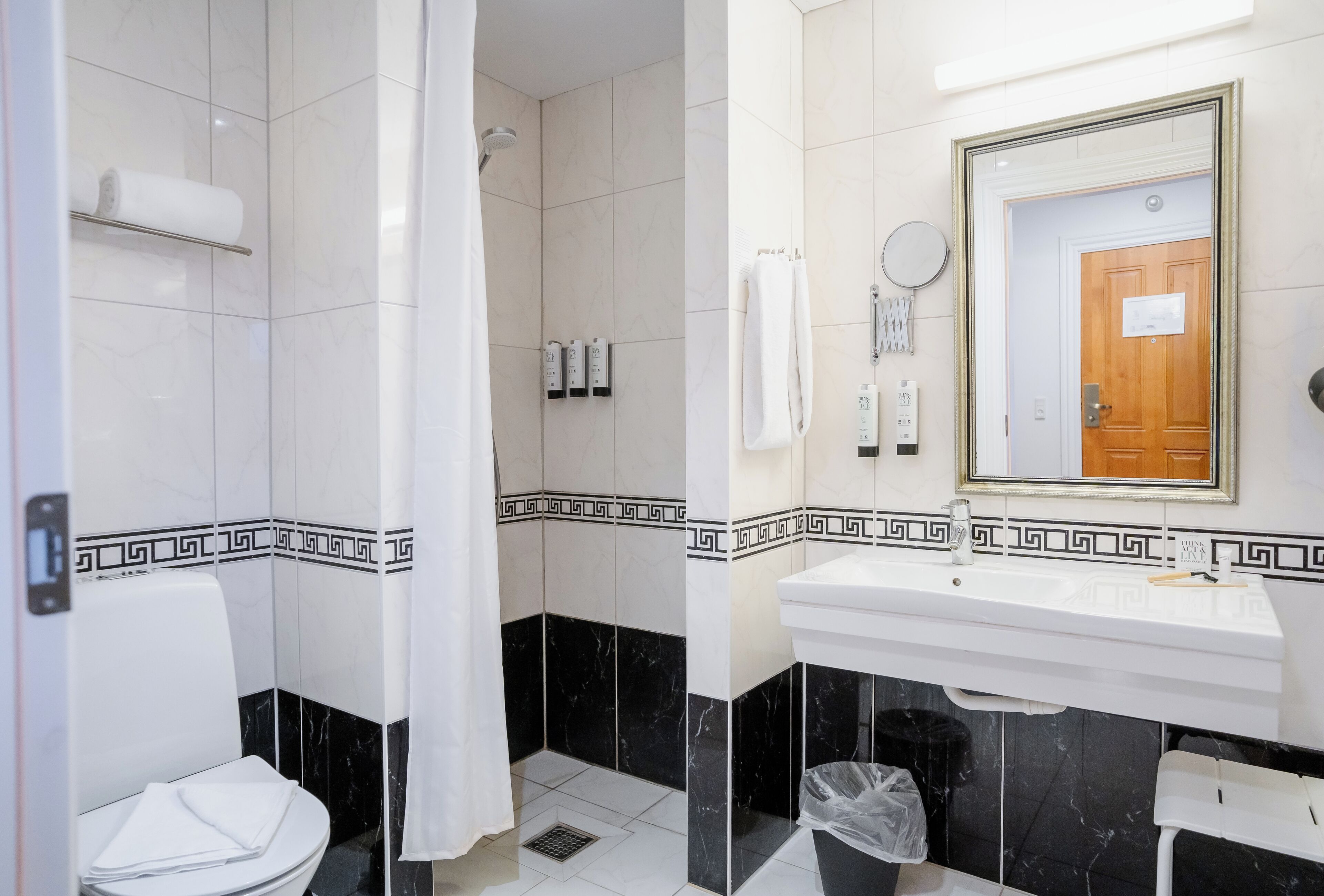 A bathroom with a toilet, shower, sink, and mirror.