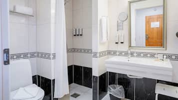 A bathroom with a toilet, shower, sink, and mirror.