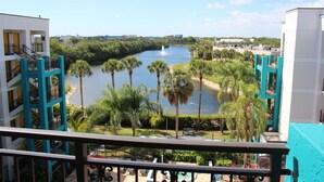 A view from a balcony overlooking a river, palm trees, and a pool area with a building in the background.