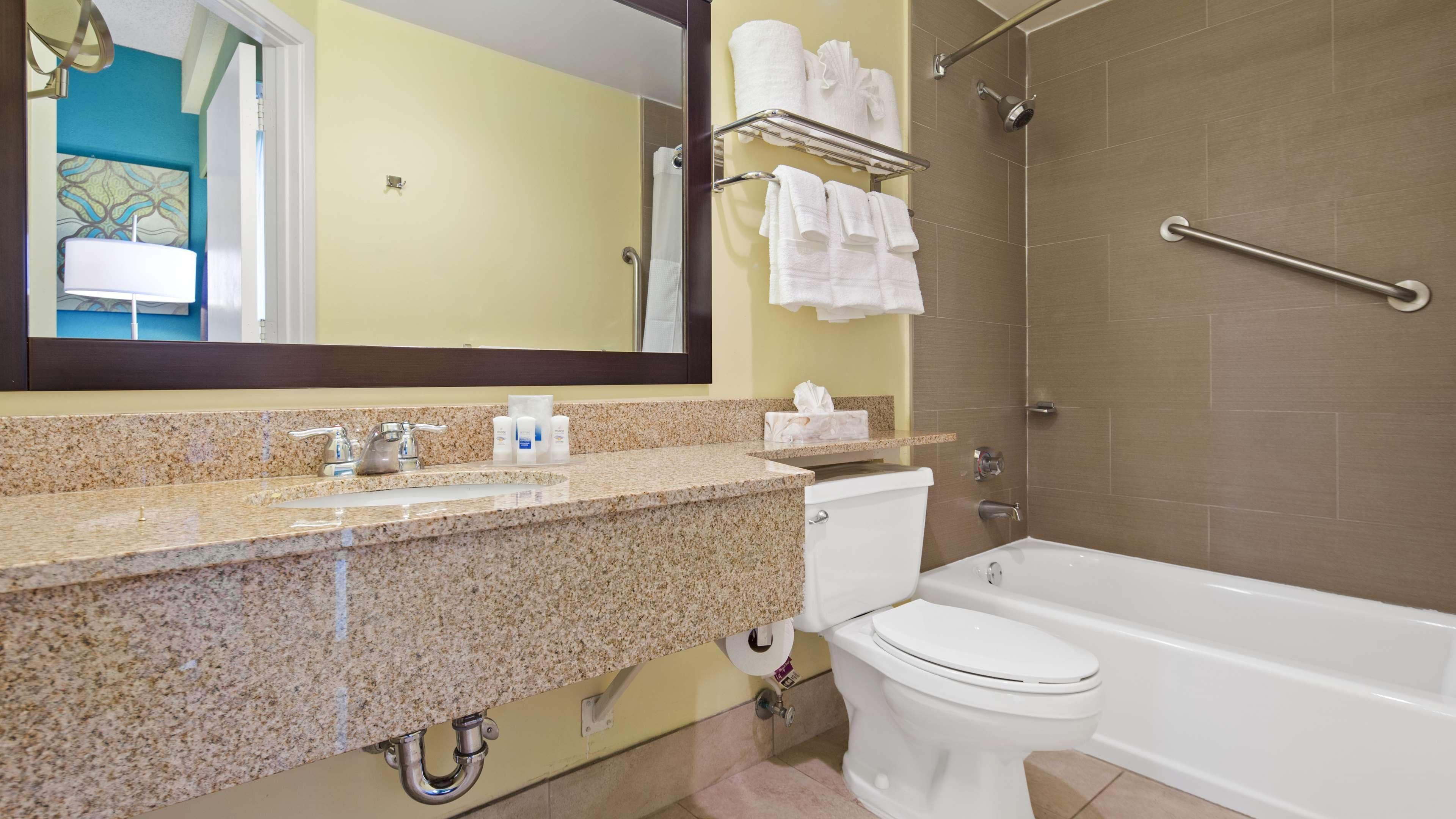 A bathroom with a granite countertop, a toilet, a bathtub, and a shower with a grab bar.