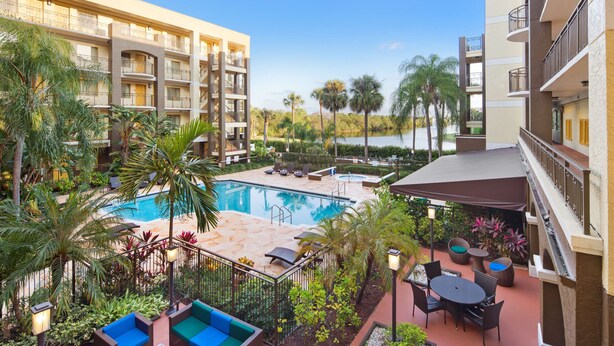 A hotel with a swimming pool surrounded by palm trees and lounge chairs.