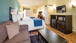 A hotel room with a bed, a sofa, a desk, a television, and a minibar.