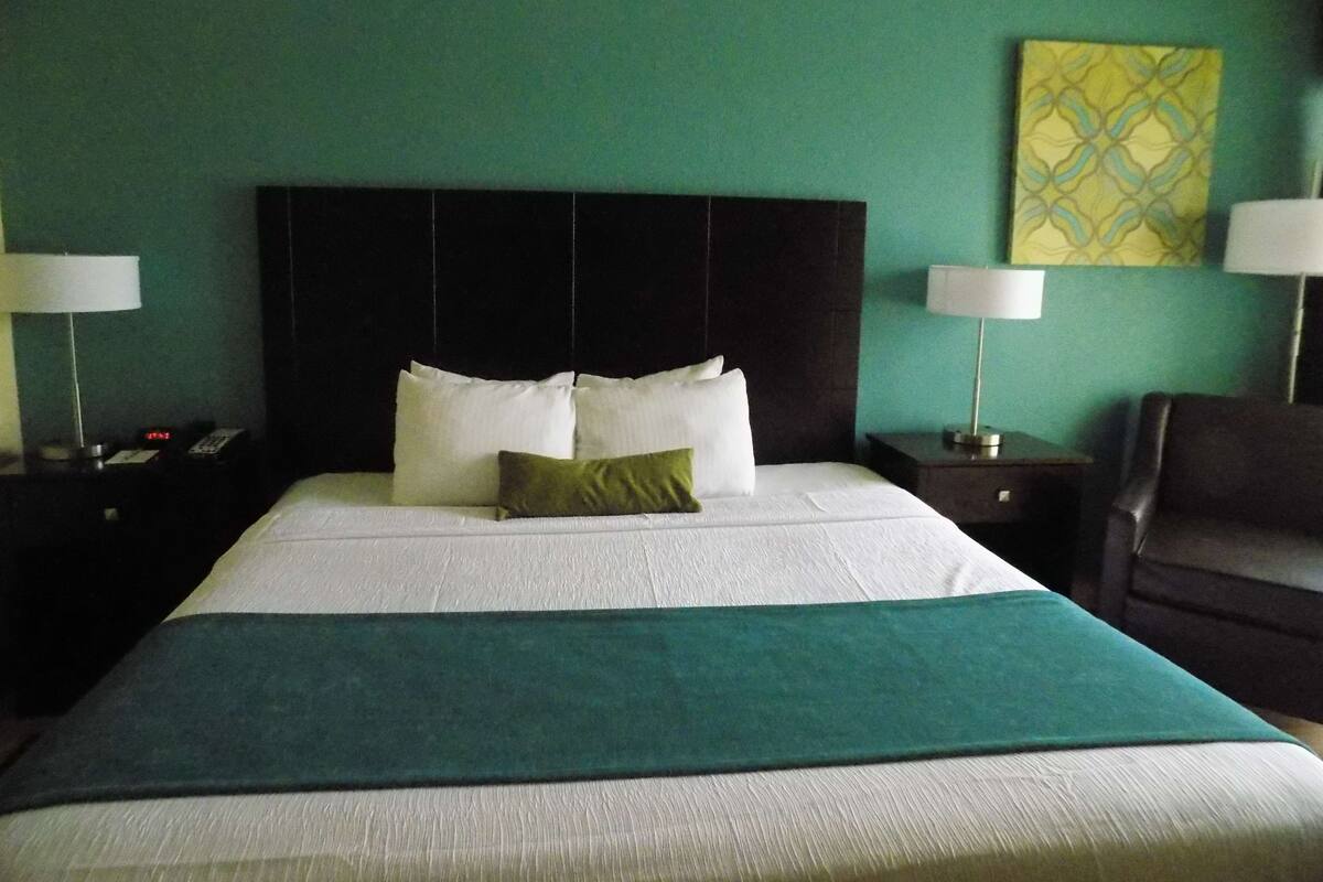 Una habitación de hotel con una cama grande, dos mesitas de noche, una pared verde y un cuadro.
