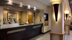 A hotel reception area with a counter, framed artwork, and modern lighting fixtures. - Embassy Suites by Hilton Kansas City International Airport (Kansas City)