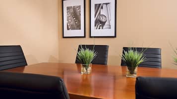 A conference room with a wooden table, four black chairs, two framed black and white photographs on the wall, and two small potted plants with green foliage.