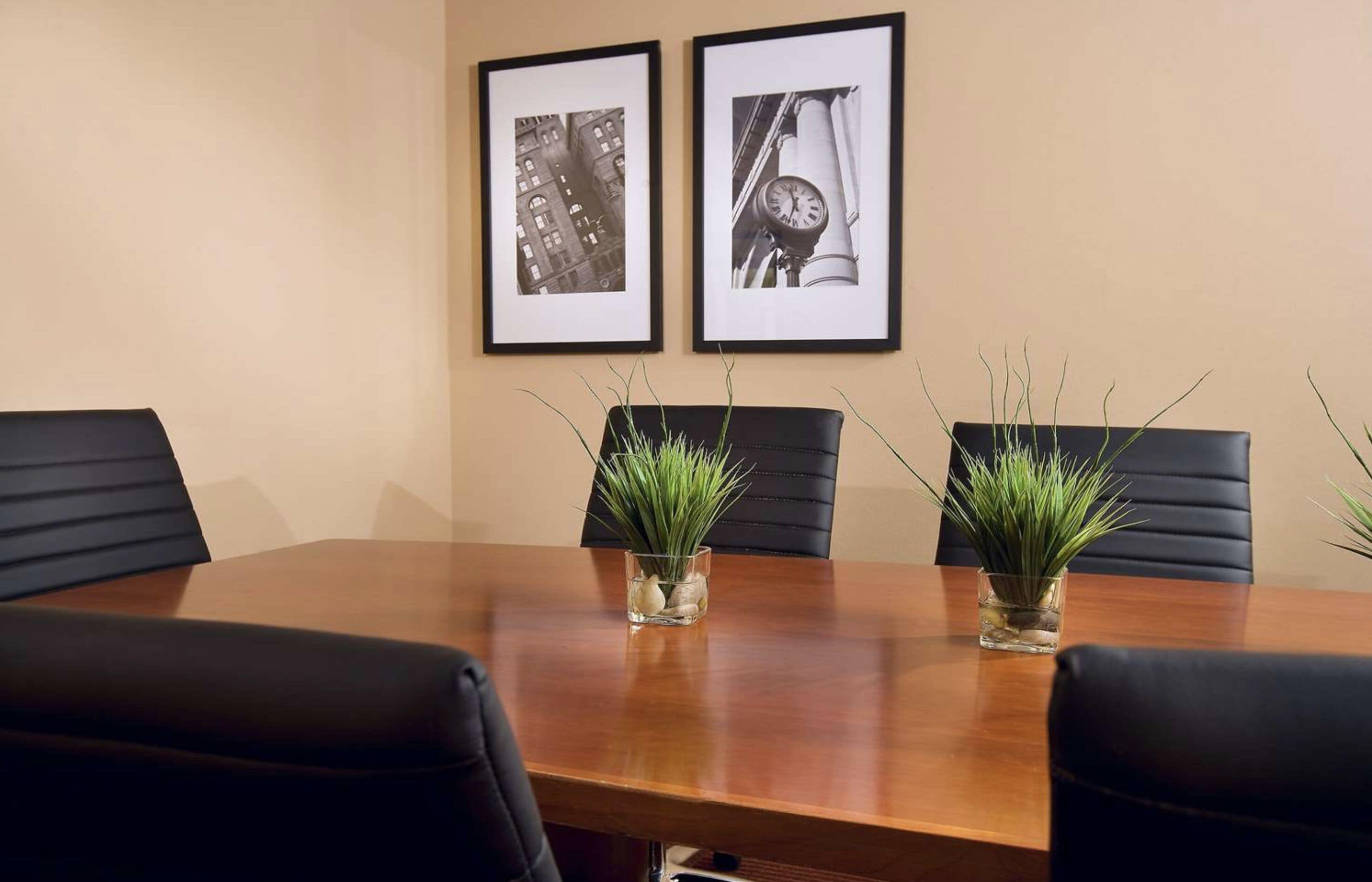 A conference room with a wooden table, black leather chairs, and two framed pictures on the wall.