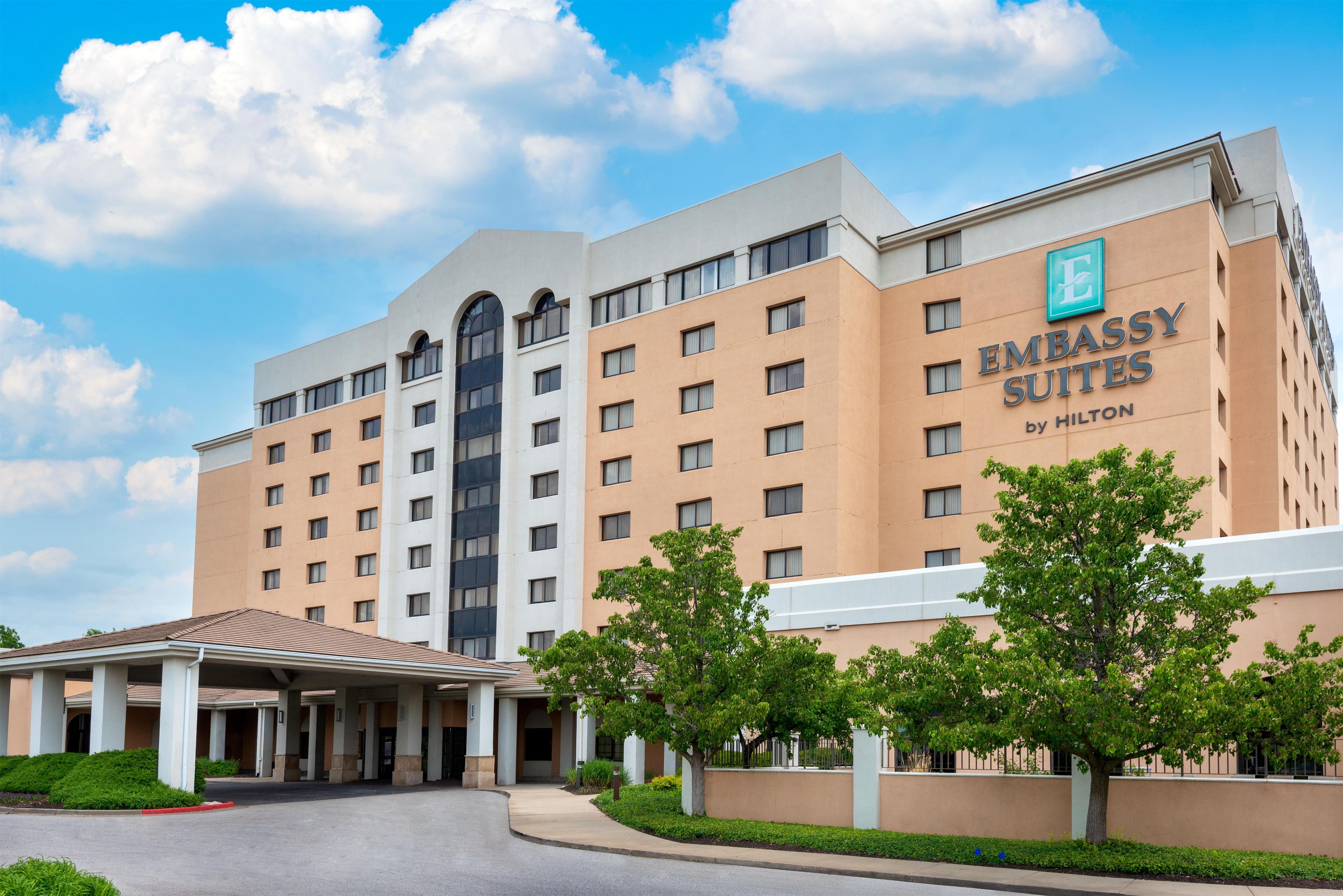 A multi-story hotel building with a prominent sign for 'Embassy Suites by Hilton' on the facade.