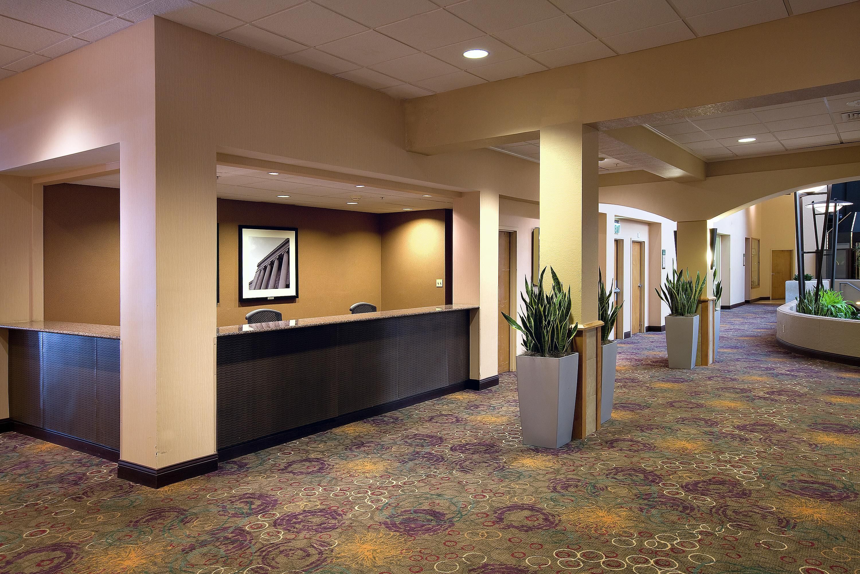 A hotel lobby with a reception desk, multiple doors, and potted plants.