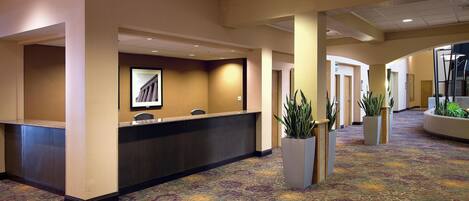 A hotel lobby with a reception desk, multiple doors, and potted plants.