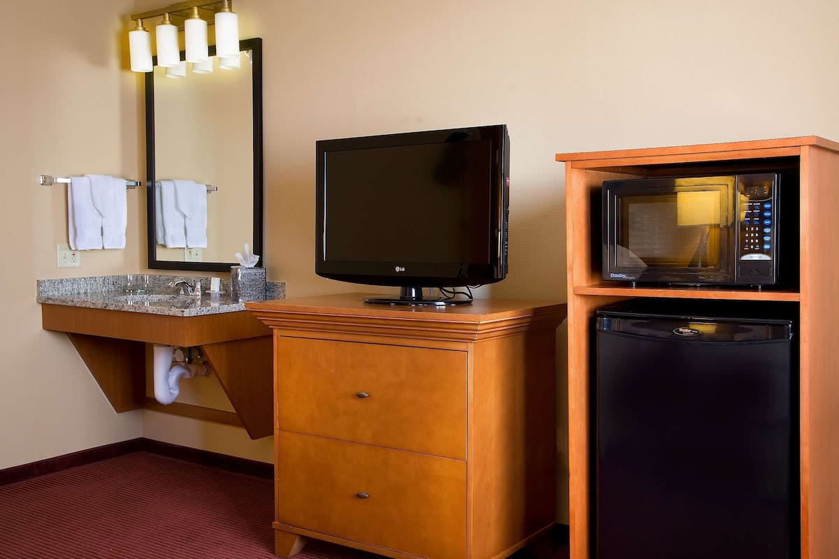 Une chambre d’hôtel équipée d’une commode en bois, d’un téléviseur à écran plat, d’un four à micro-ondes et d’une coiffeuse avec un miroir et un porte-serviettes.