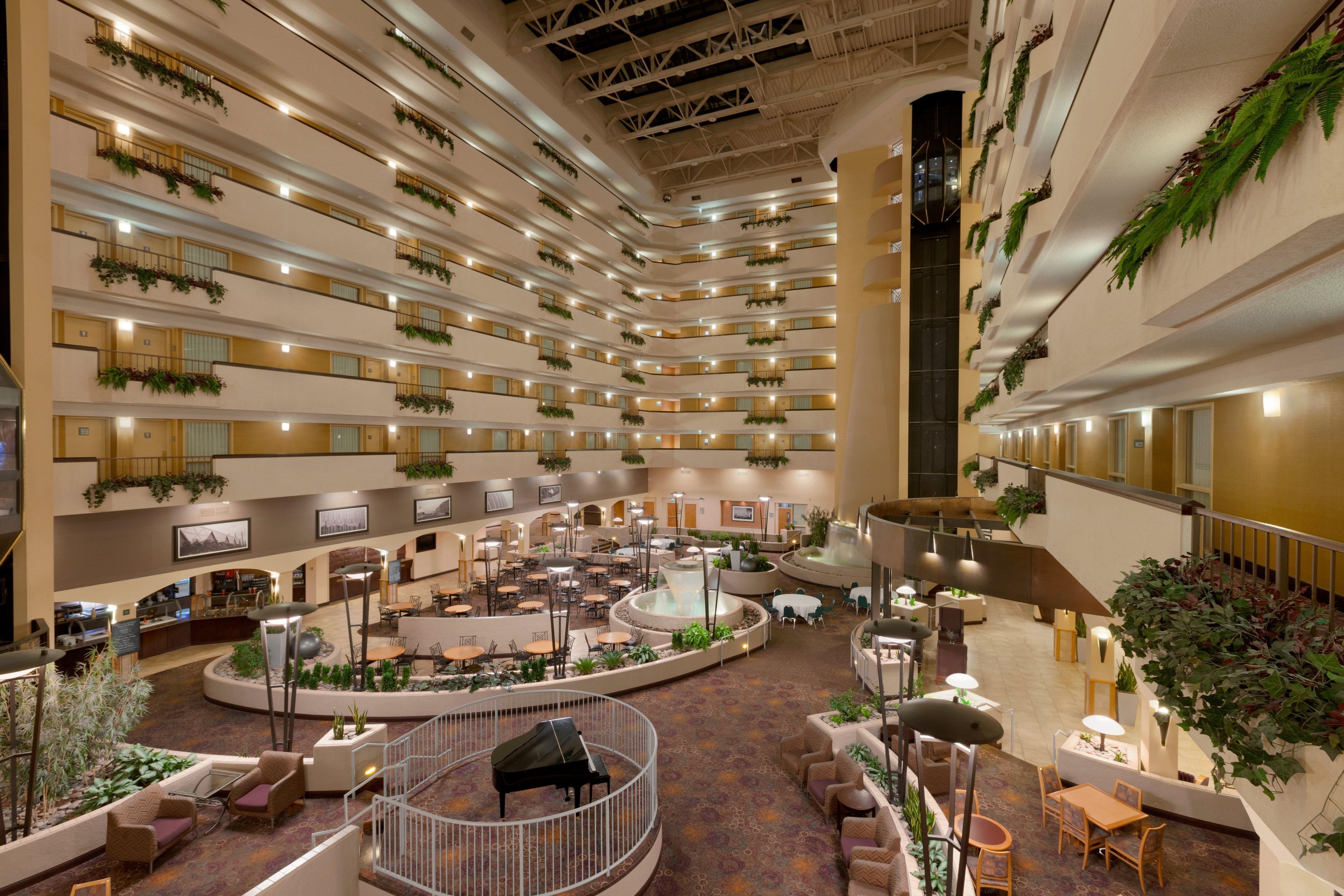 A multi-level hotel atrium with a central water feature, multiple dining areas, and balconies with greenery.