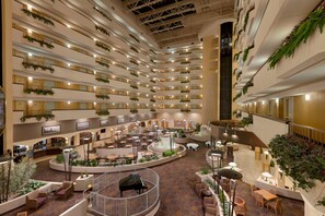 A multi-level hotel atrium with a central water feature, multiple dining areas, and balconies with greenery. - Embassy Suites by Hilton Kansas City International Airport (Kansas City)