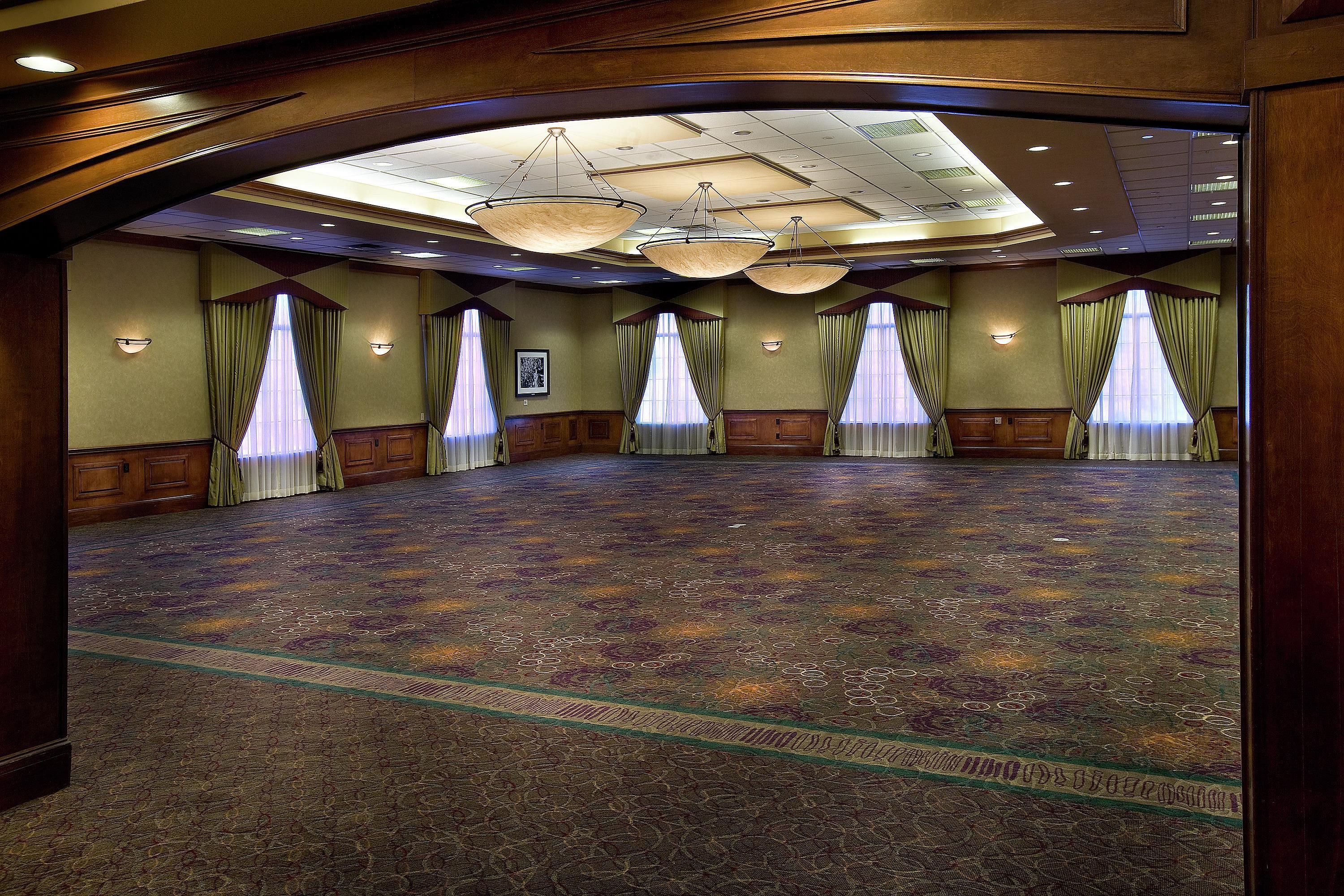 A large conference room with a patterned carpet, wooden paneling, and a high ceiling with chandeliers.