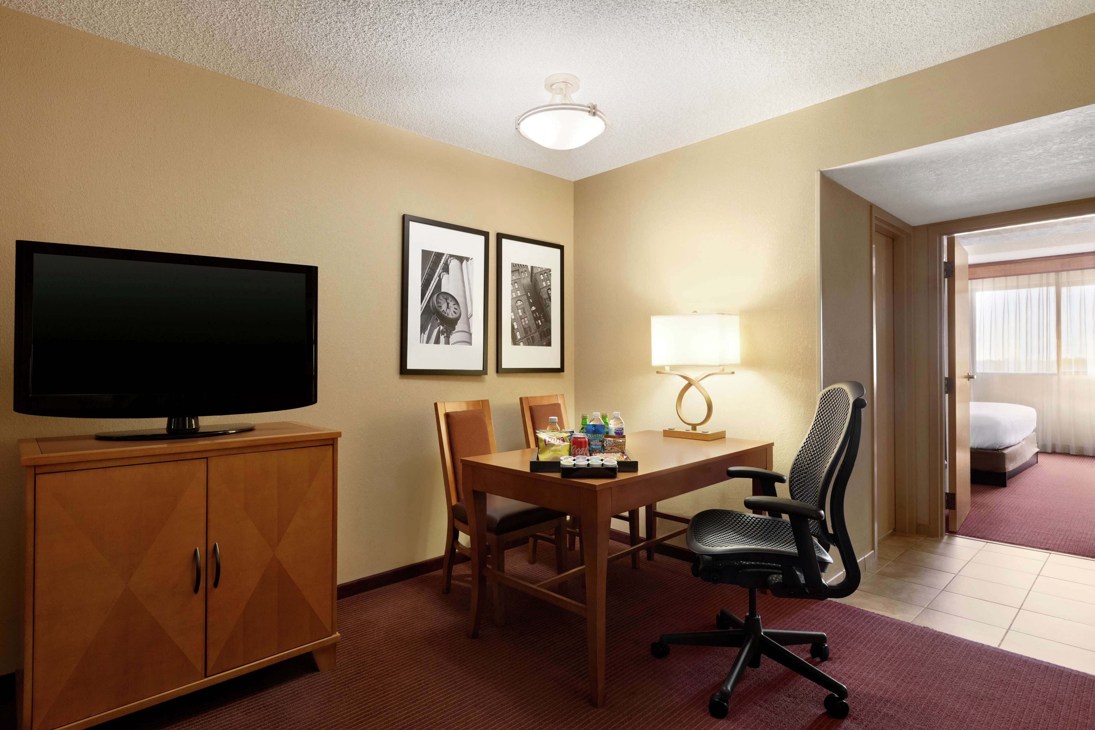 Une chambre d’hôtel avec une télévision, un bureau avec une lampe, deux tableaux encadrés et un lit.