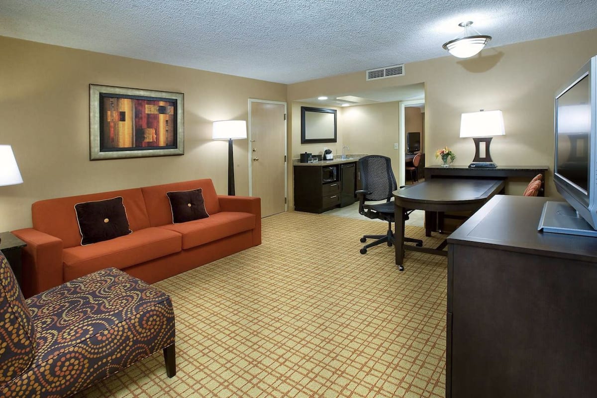 Une chambre d’hôtel équipée d’un canapé, d’un fauteuil, d’un bureau, d’une télévision et d’une kitchenette.