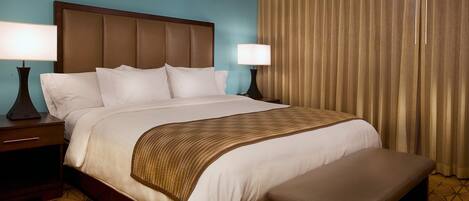 A hotel room with a large bed, two bedside tables, a bench, and a window with curtains.