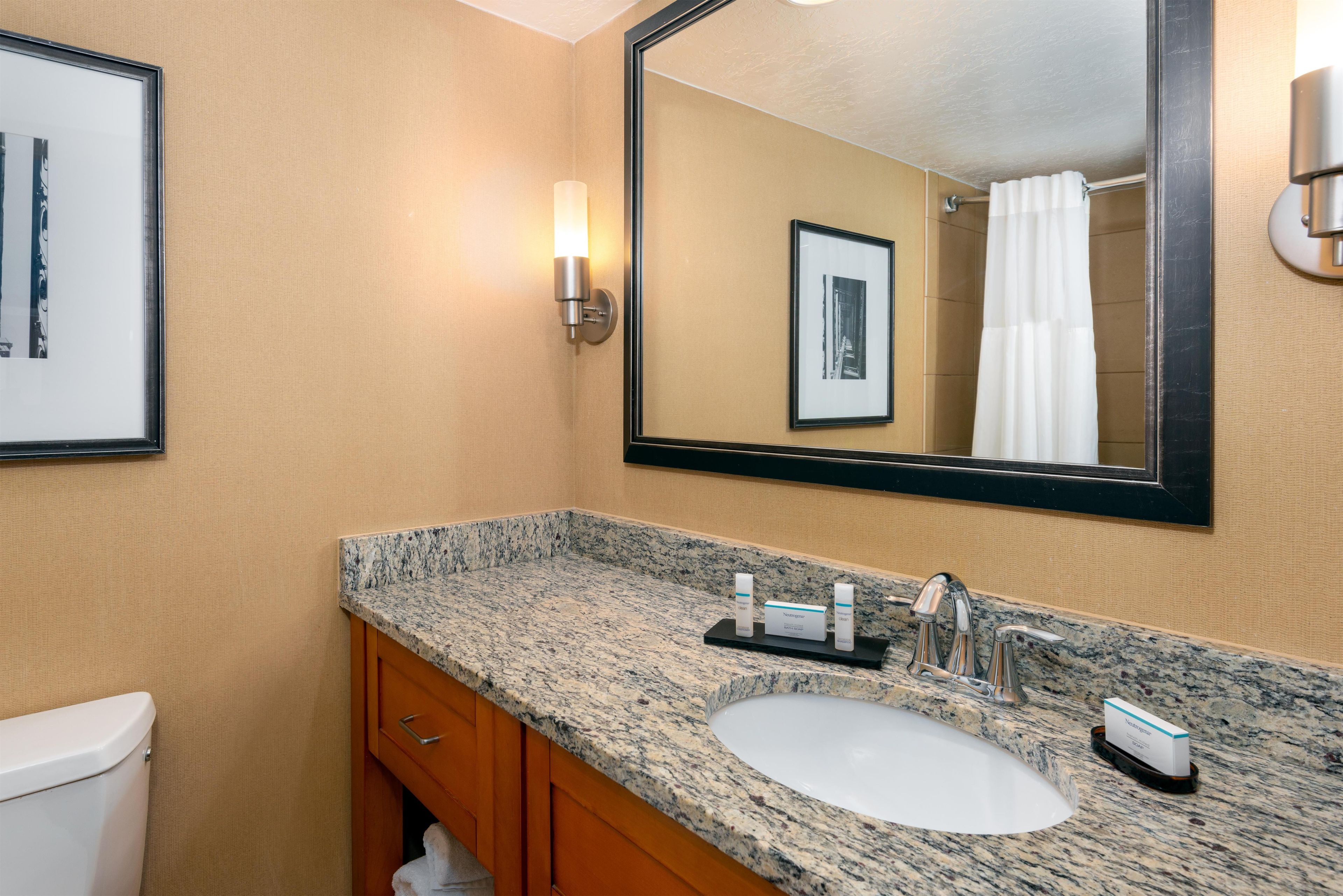 A bathroom with a granite countertop sink, a mirror, framed pictures on the wall, and a shower curtain.