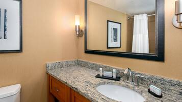A bathroom with a granite countertop sink, a mirror, framed pictures on the wall, and a shower curtain.