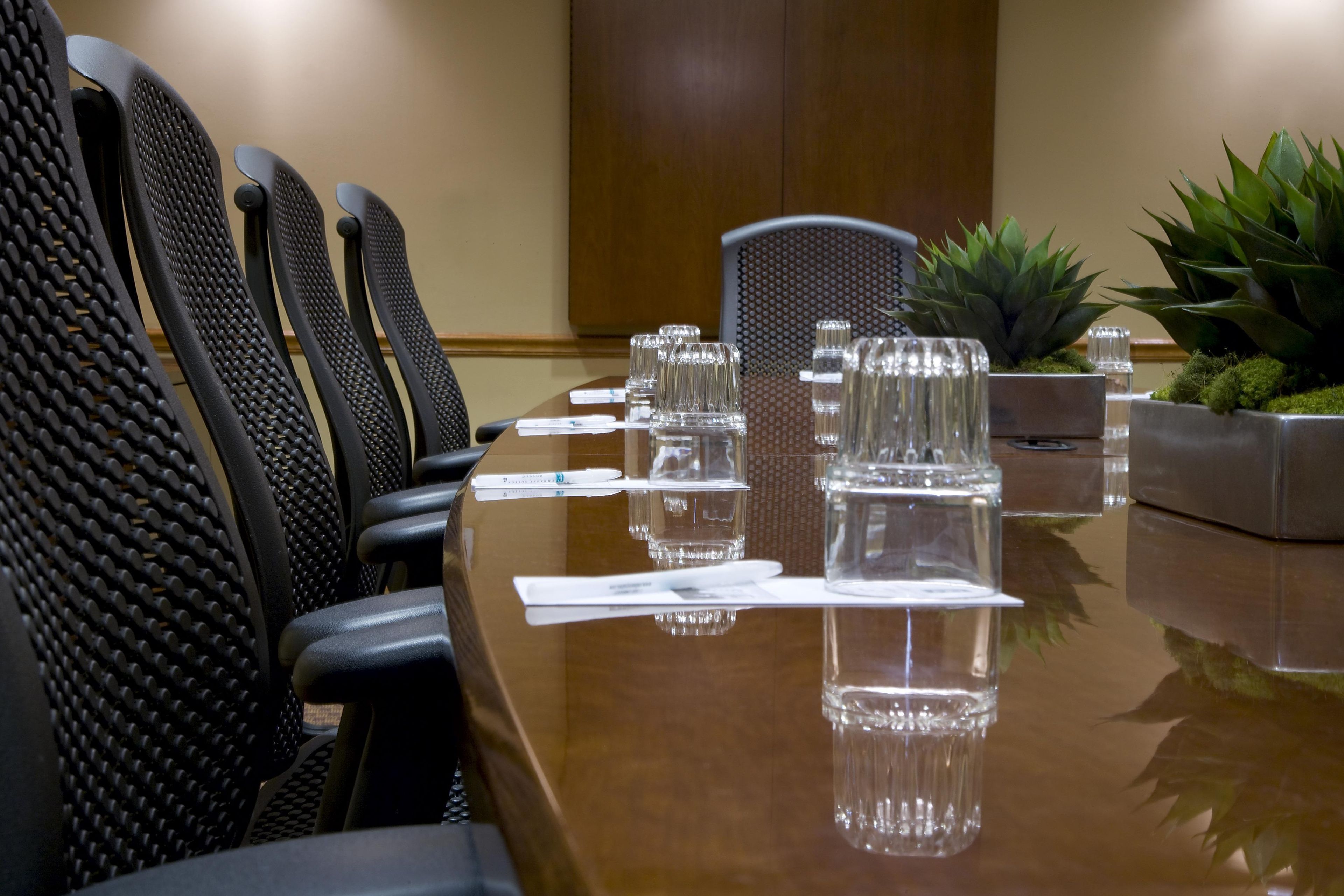 Une salle de conférence avec une longue table, des chaises noires, de la verrerie transparente et une plante en pot.