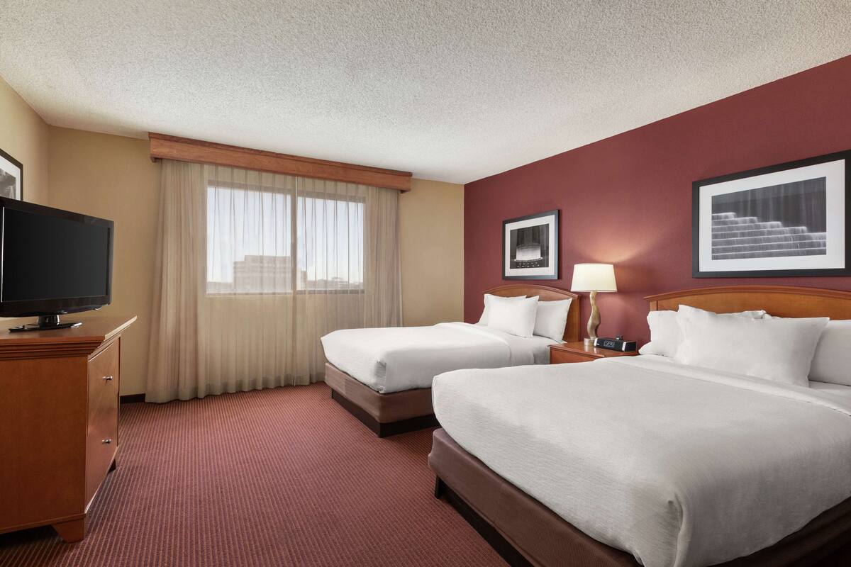 Une chambre d’hôtel avec deux lits, une télévision, un bureau et une fenêtre avec des rideaux.